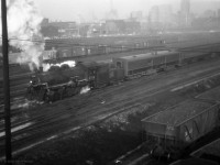 CN 8304 is a class P-5-a 0-8-0 switcher, moving coaches near Spadina Road in downtown Toronto.<br>
Built by ALCo in December 1923, last in a batch of 5 for the GTW, it was transferred to CN in 1942.<br> 
It survived through the end of steam on CN, scrapped in 1961. <br><br>
Its first car appears to be lettered "EXPRESS", beyond it are clerestory roof coaches.<br>
At bottom right is a GM&O hopper car, could be a coal load for the nearby Spadina coaling tower.<br><br>
The switcher's exhaust and vapour suggest that it is reversing toward Toronto Union Station.
